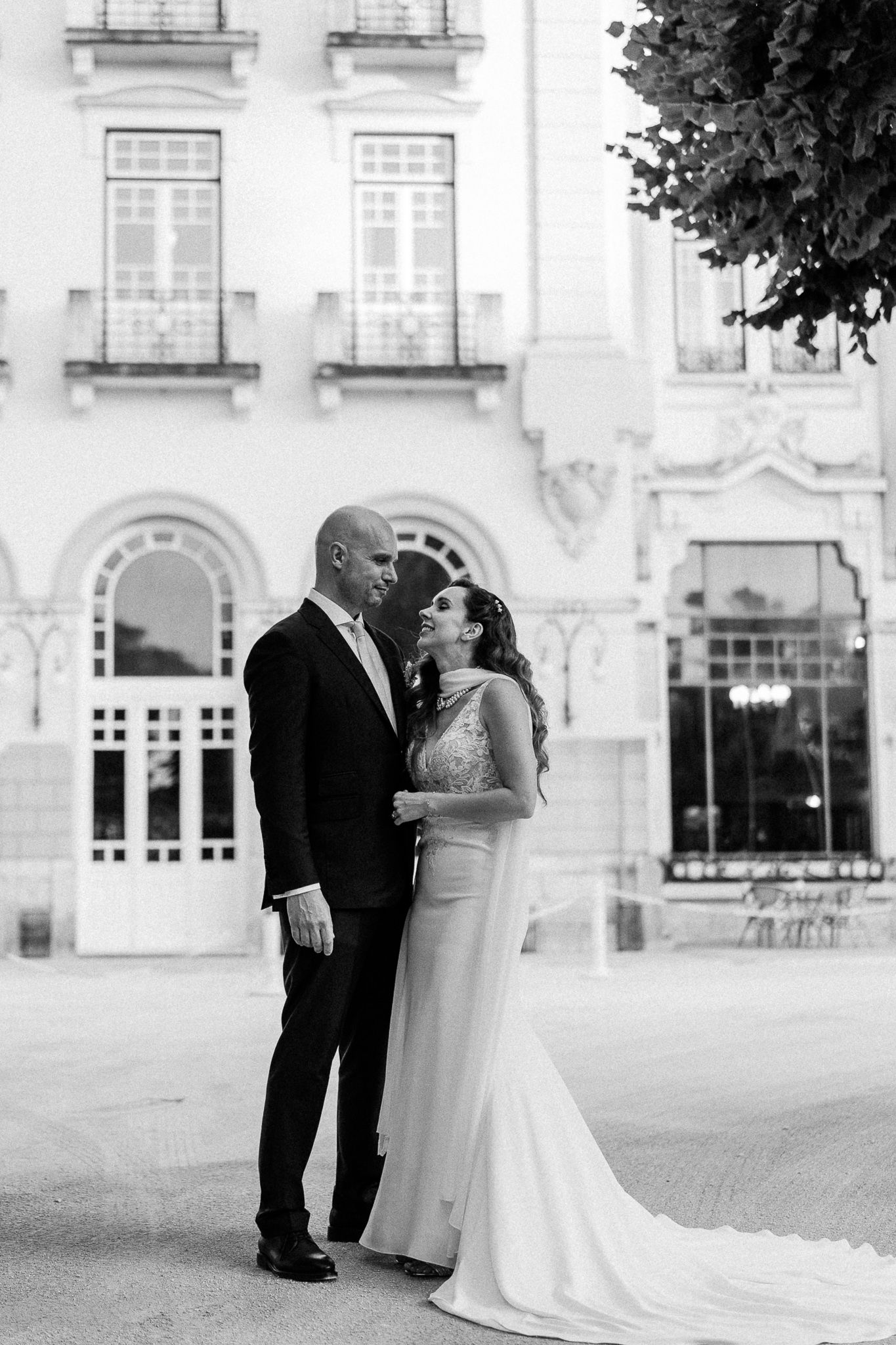 Black and white wedding photo of bride and groom gazing at each other outside an elegant European building.