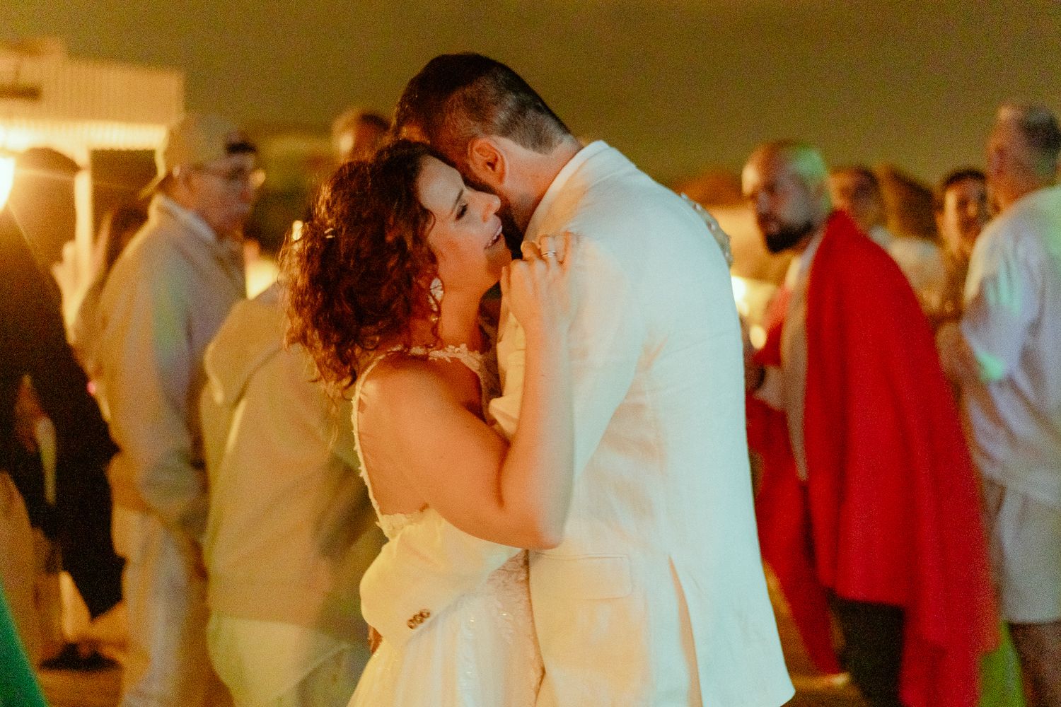 Couple sharing a romantic first dance kiss at their wedding reception in warm golden lighting.