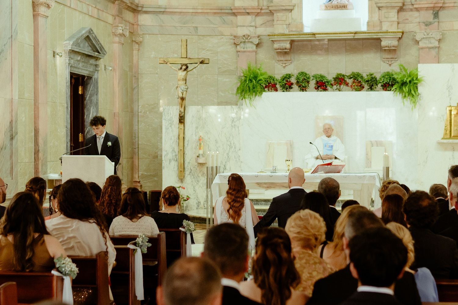 Elegant church wedding ceremony with guests seated in pews as officiant leads service beneath ornate altar.