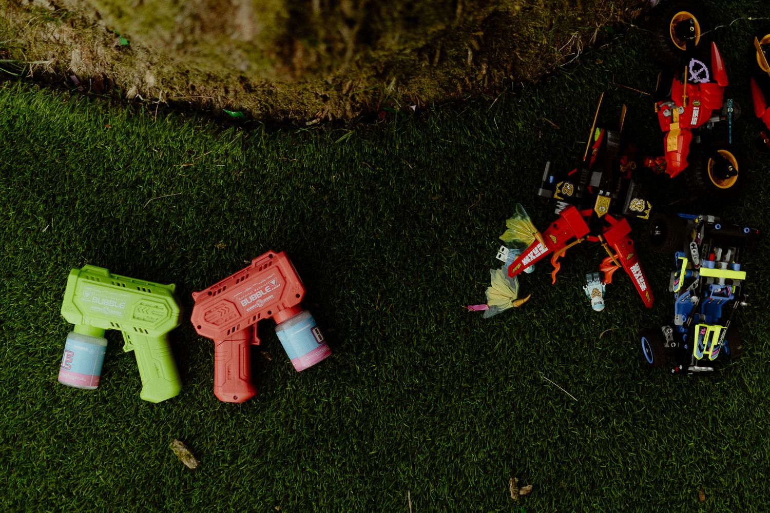 Two colorful toy water guns and a red Lego robot set on green grass outdoors.