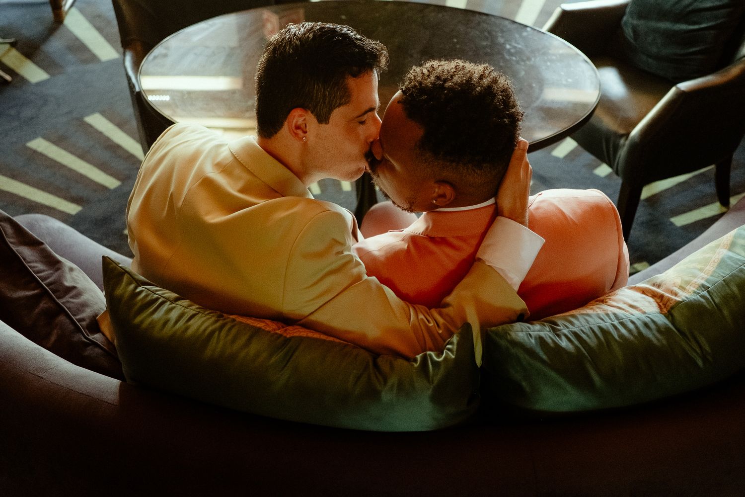 Two men sharing an intimate moment cuddling together on a green bean bag chair in a cozy lounge setting.