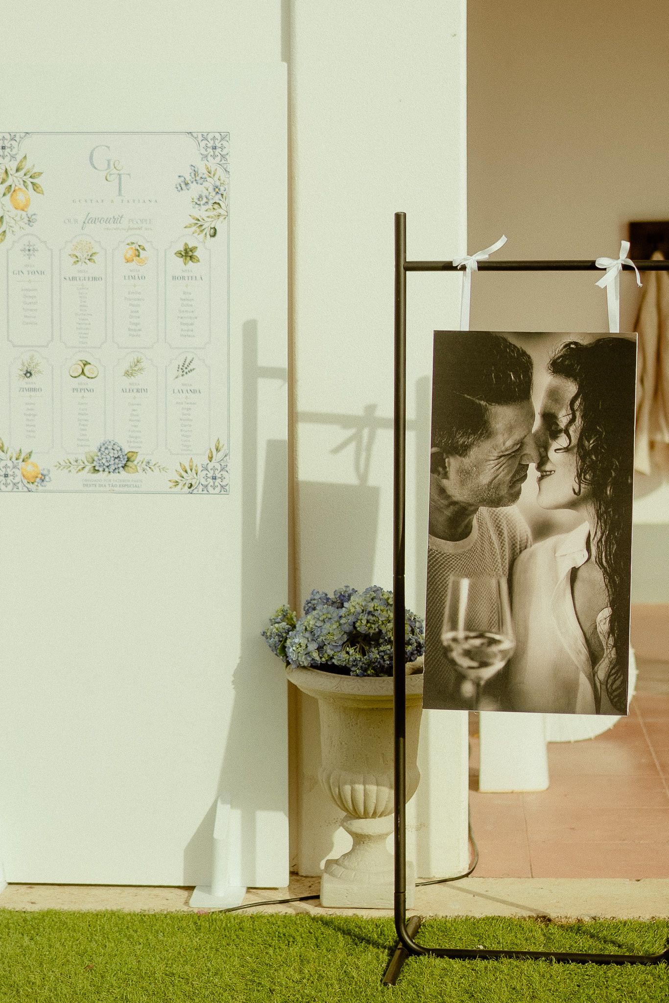 Elegant wedding seating chart display with floral design beside a black and white couple photo on a metal stand at outdoor venue.