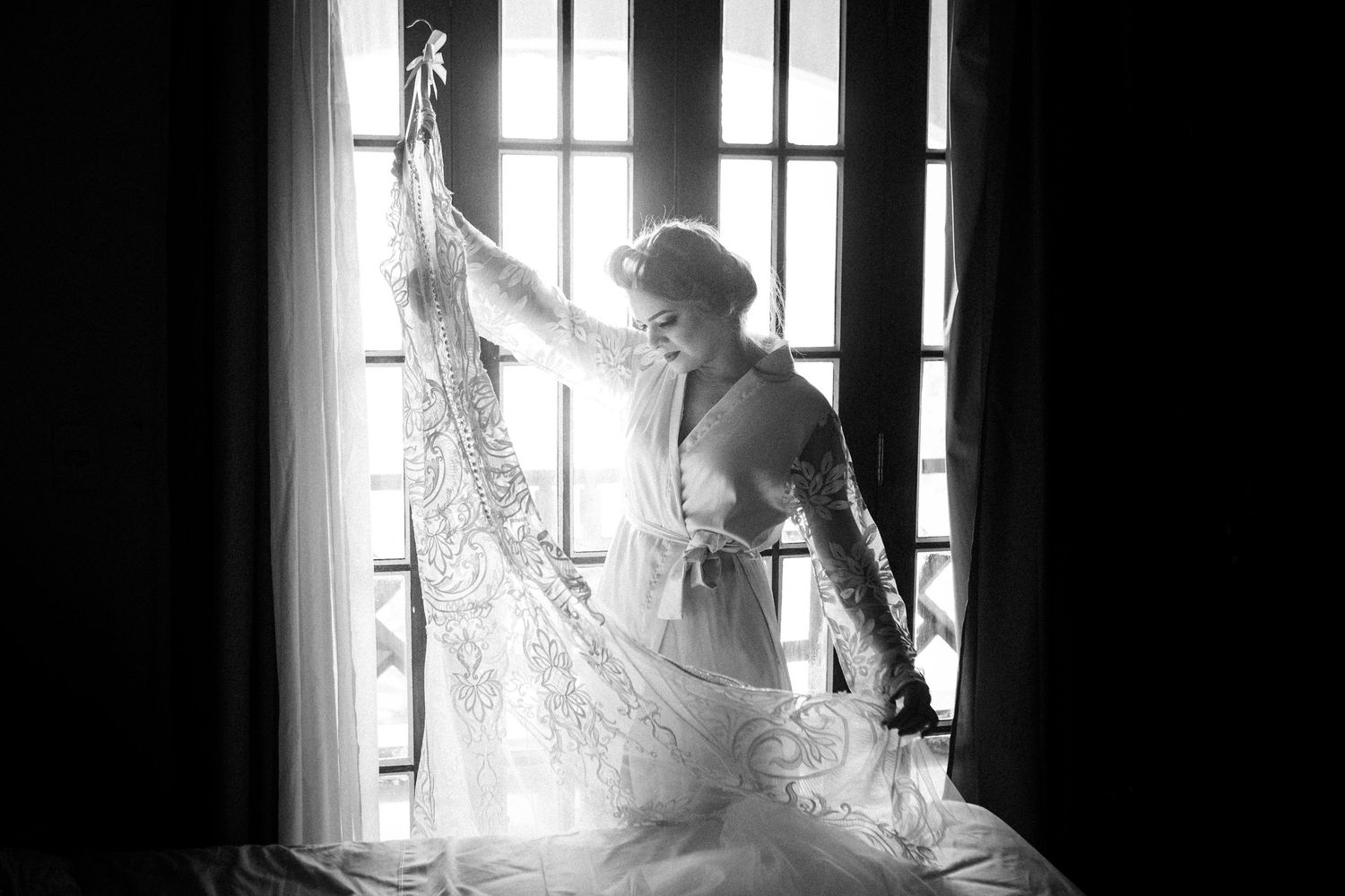A dark silhouette stands by a sunlit window in a moody black and white interior scene.