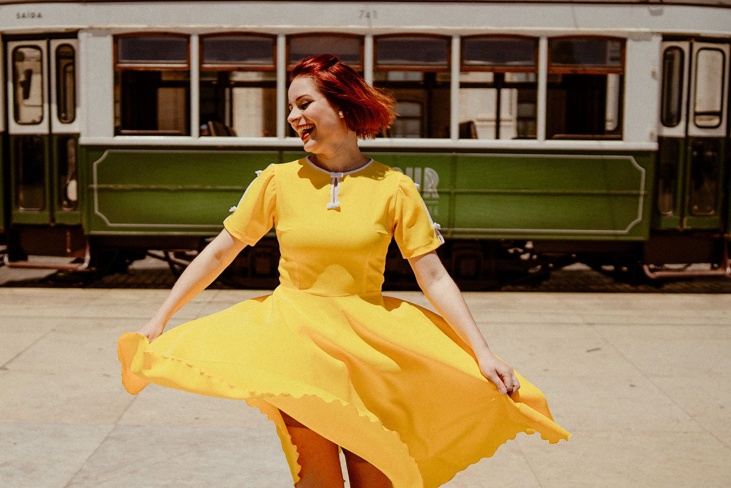 A bright yellow vintage-style dress flows in the breeze beside a classic green tram.