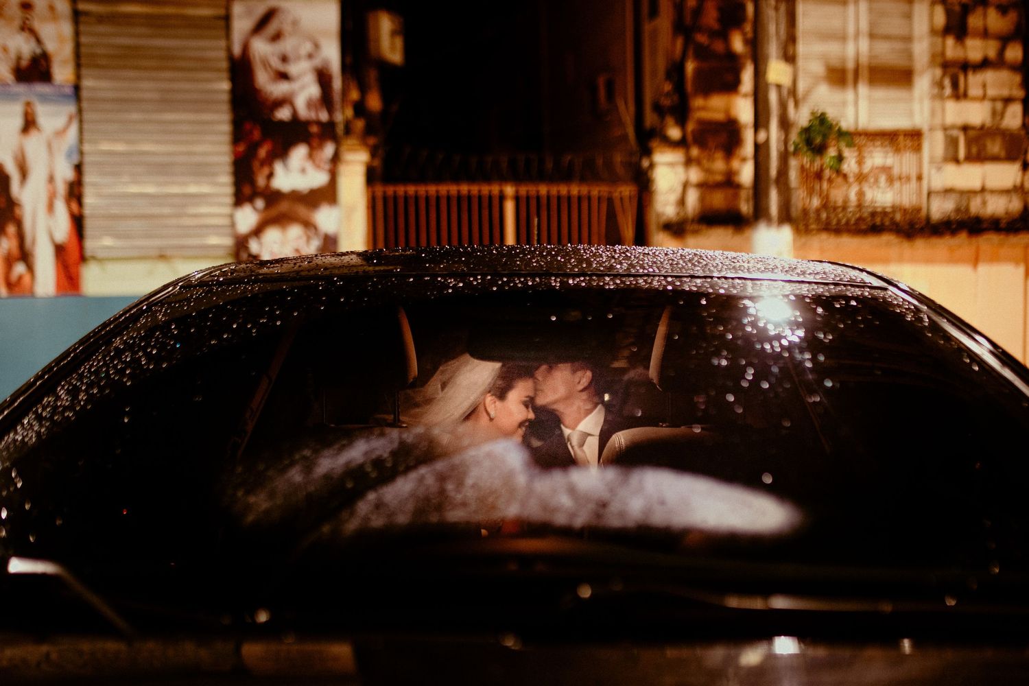Silhouette of a couple kissing through a car windshield at night.