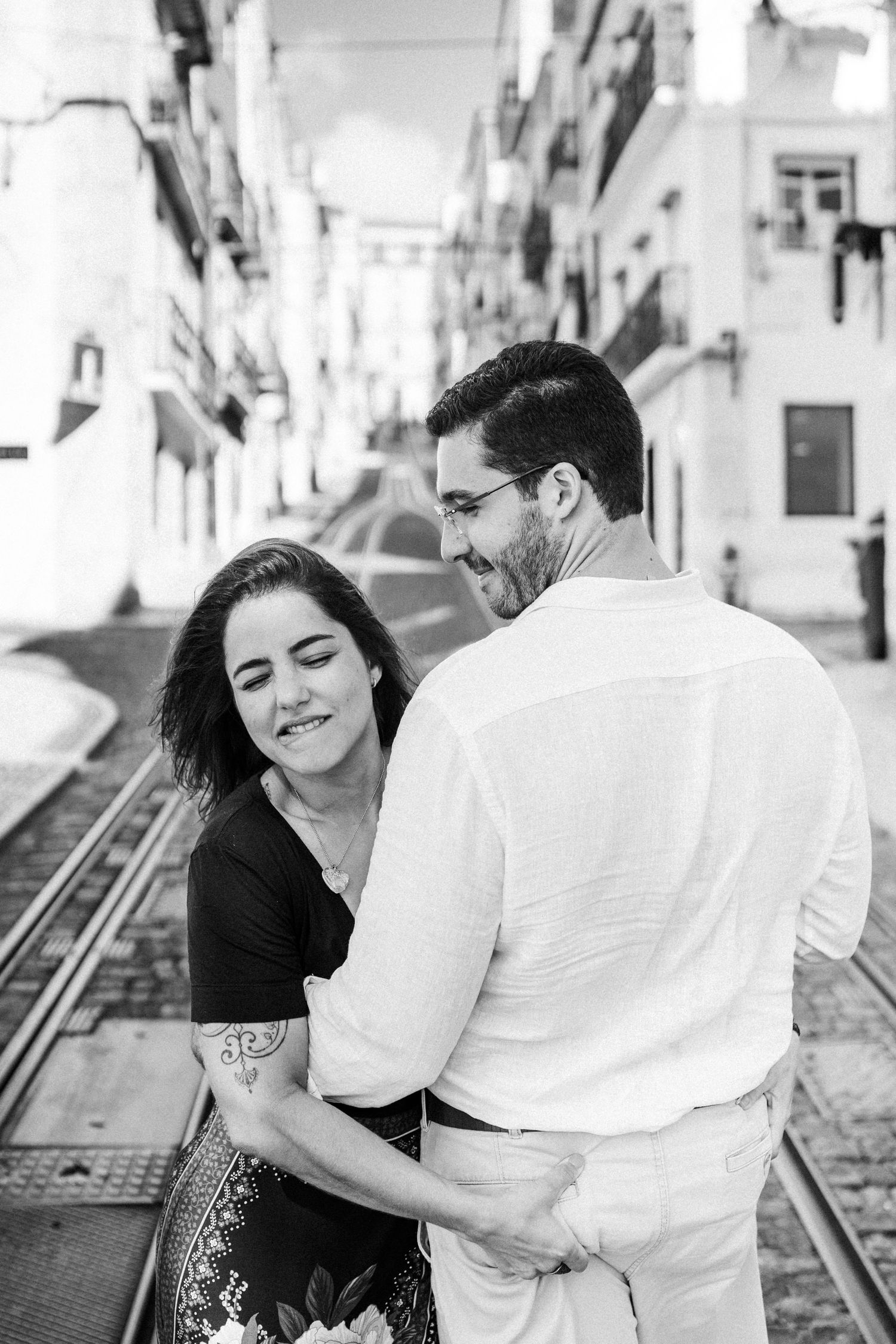 A couple share intimate moments on a sun-lit cobblestone street, captured in a series of black and white photographs.
