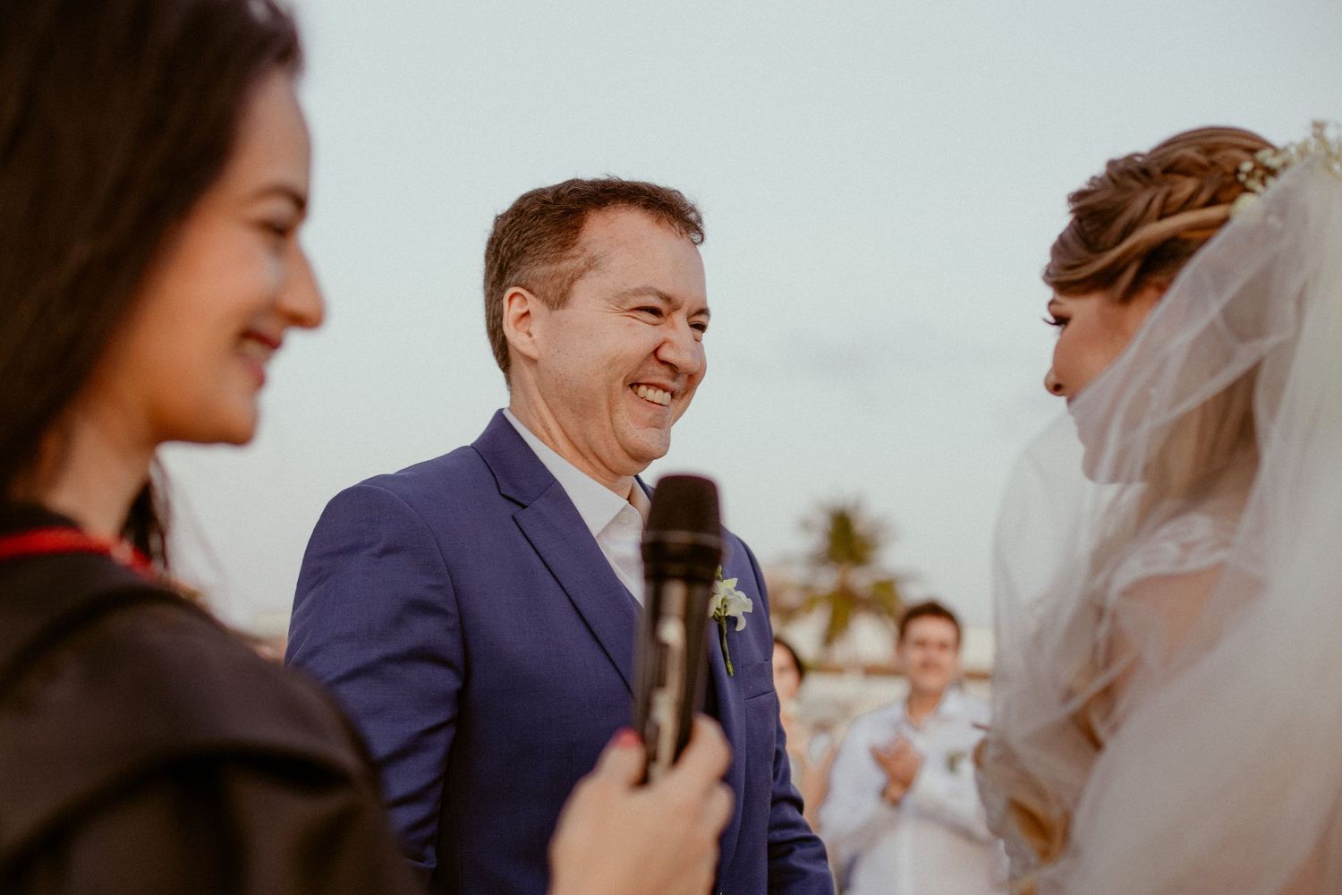 Wedding ceremony participants share a joyful moment during outdoor vows with palm trees in background.