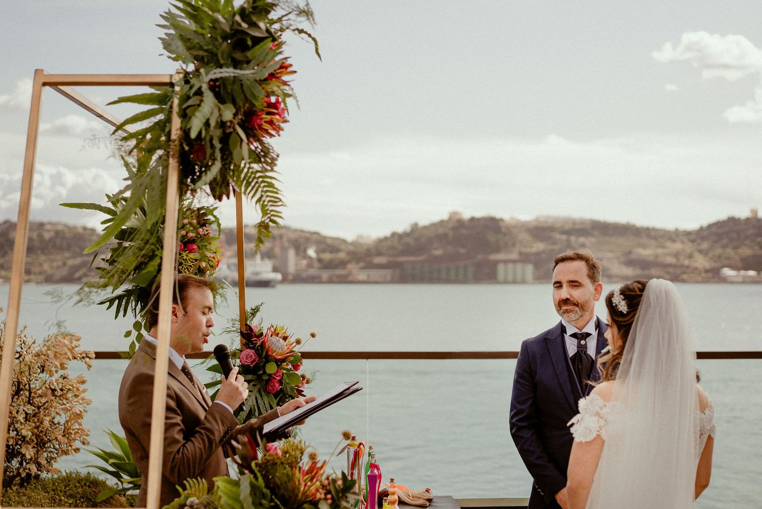 A beachside wedding ceremony in the tropics with palm trees and floral decorations along a wooden aisle.
