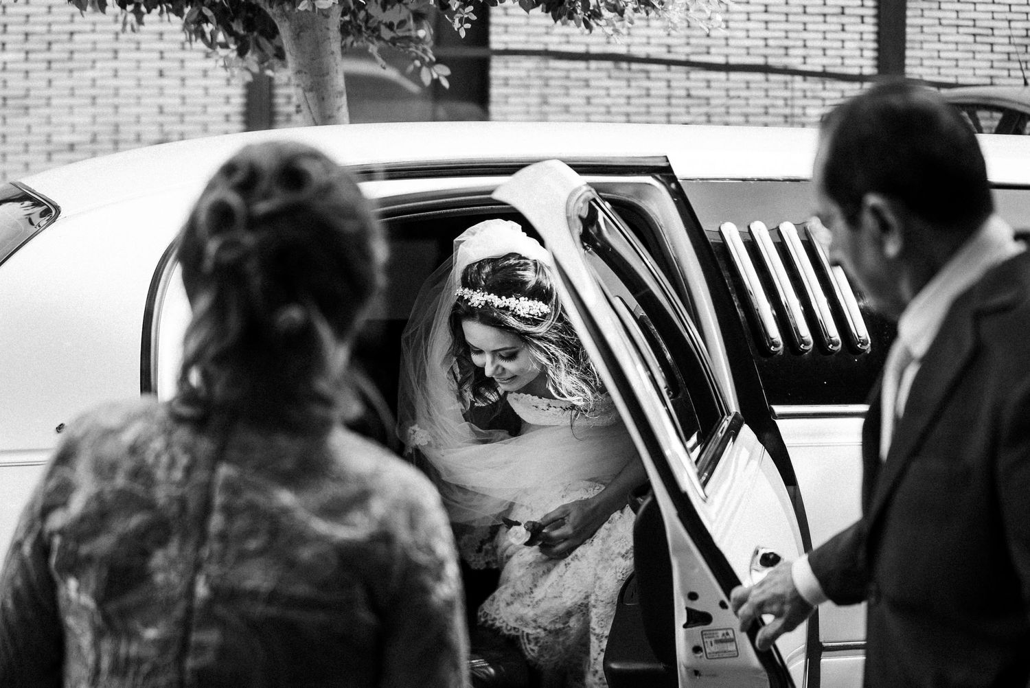 Black and white photo of wedding party assisting with limousine entrance.