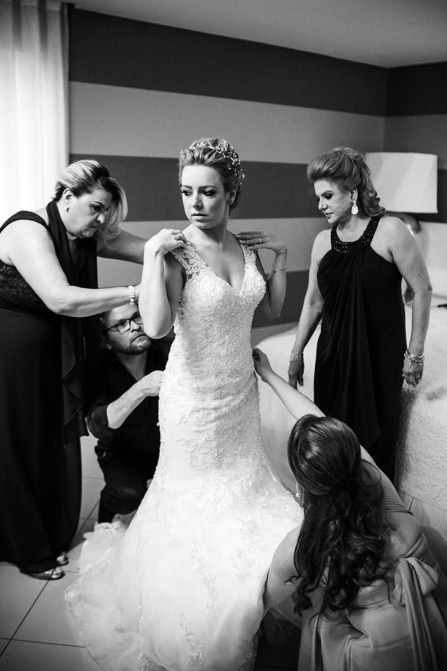 A bride in a fitted lace wedding gown gets help from attendants during final preparations.