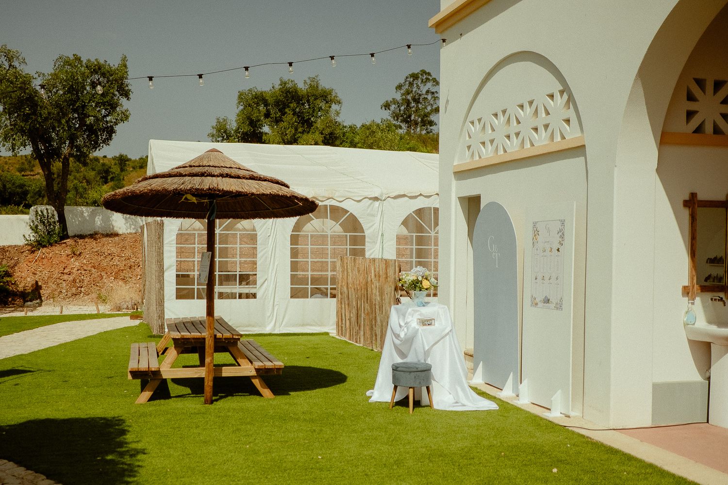Elegant outdoor wedding venue with thatched umbrella, picnic table, and decorated table on manicured lawn.