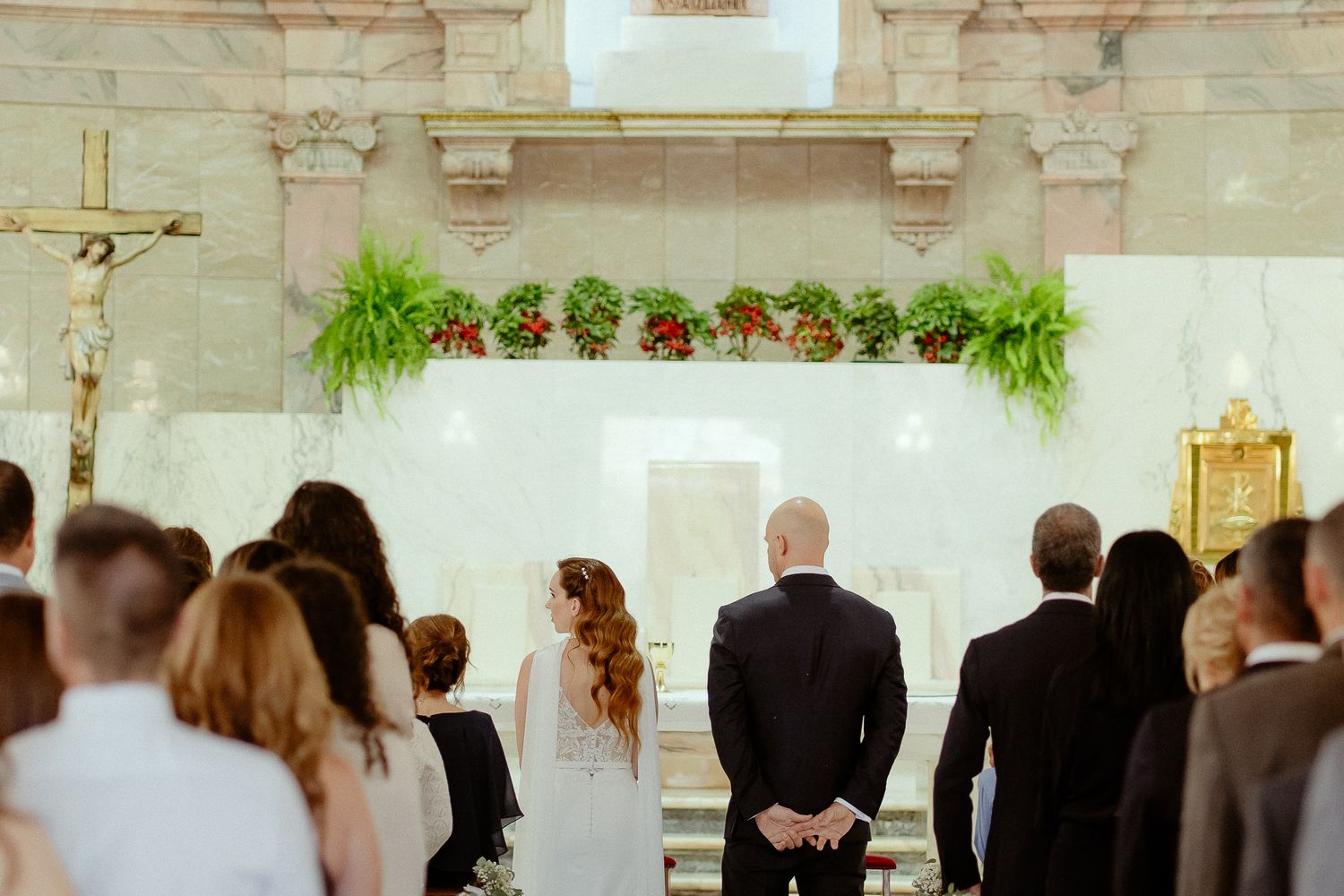 Bride and groom stand at church altar during wedding ceremony with floral decorations and guests seated in pews.