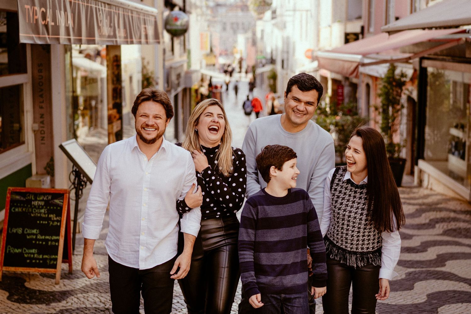 A group of people walking and smiling together on a charming European cobblestone street lined with shops and cafes.
