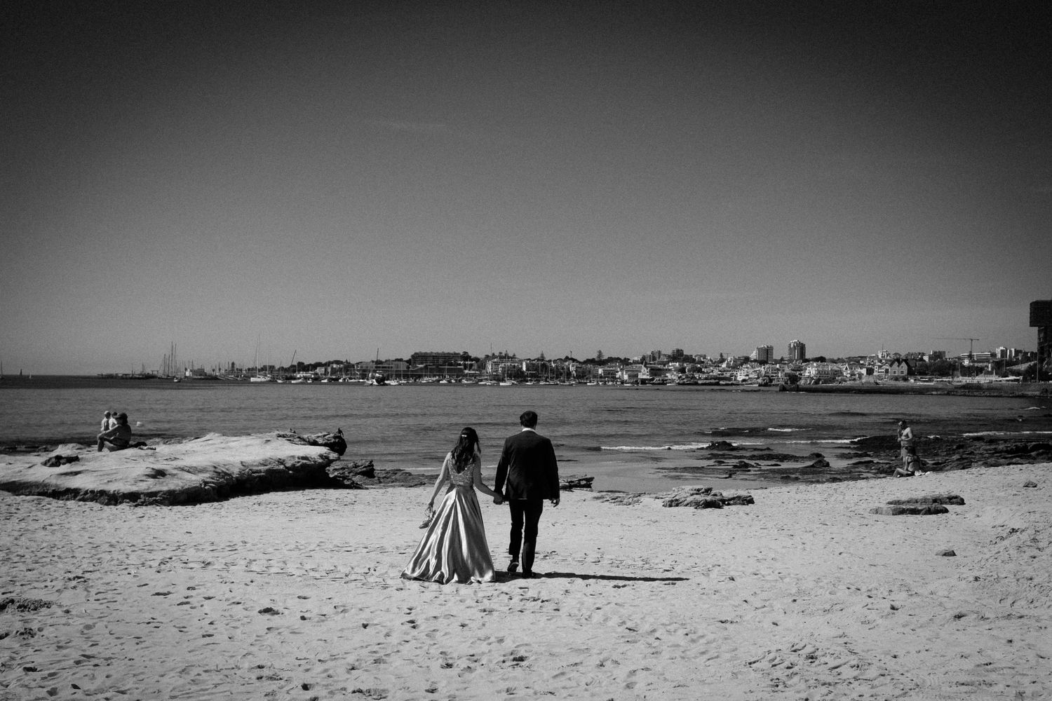 A black and white panoramic sequence of a beach scene with silhouettes walking along the shoreline at sunset.