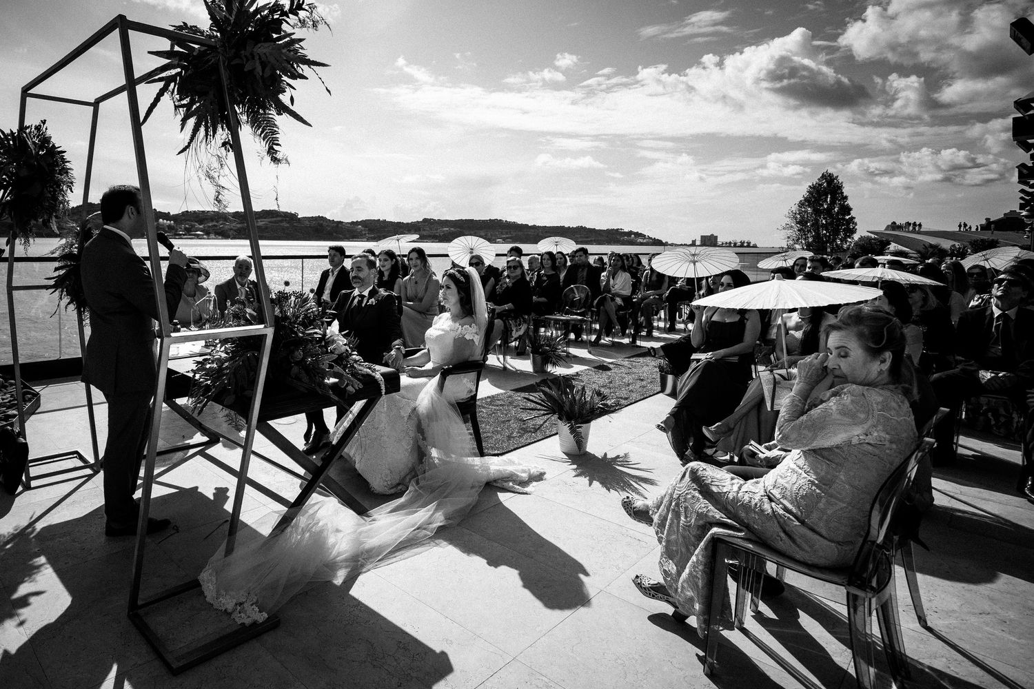 Black and white photo of outdoor waterfront wedding ceremony with guests seated.