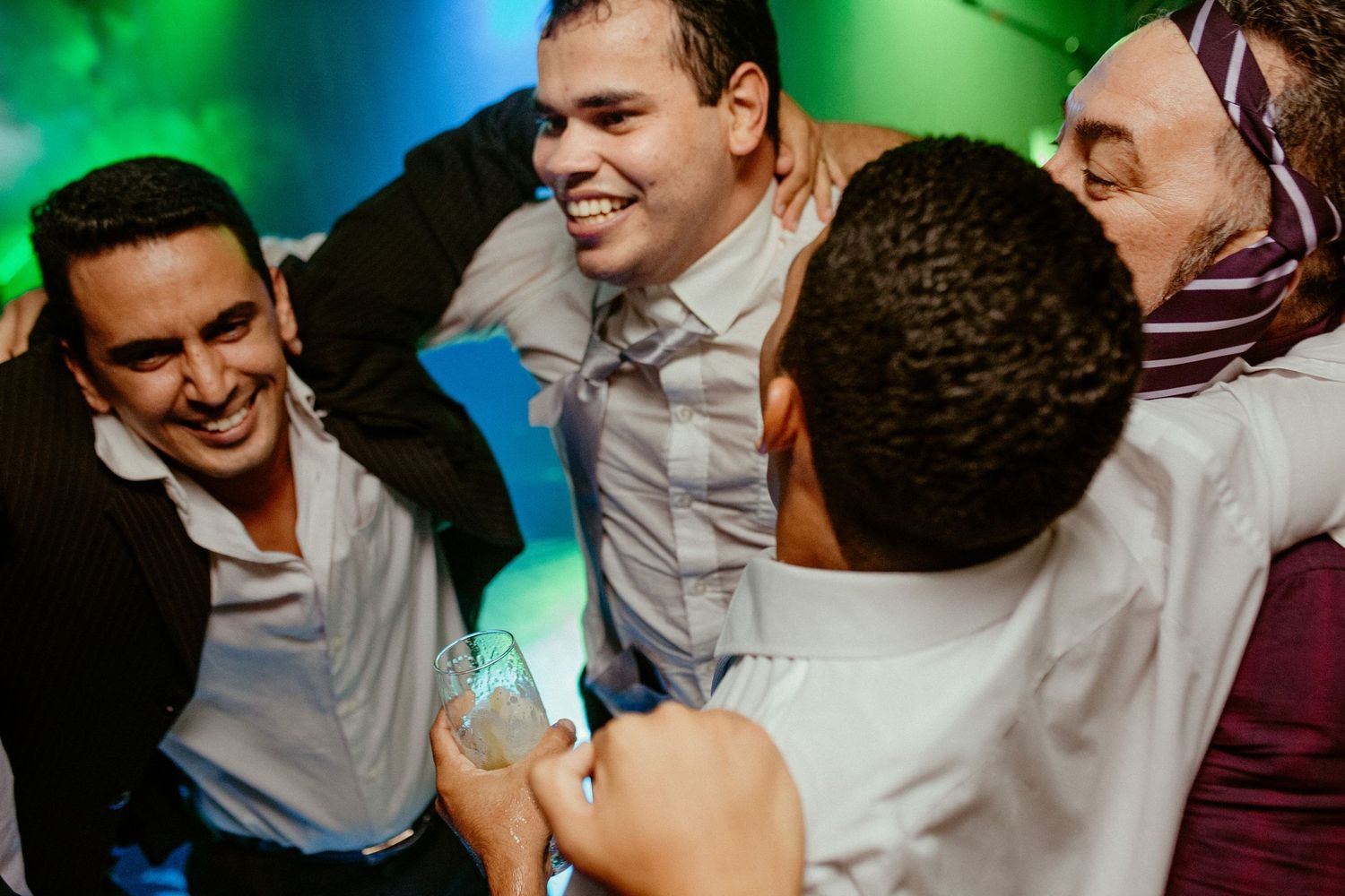 Wedding guests dancing and celebrating with energetic expressions under colorful party lights.