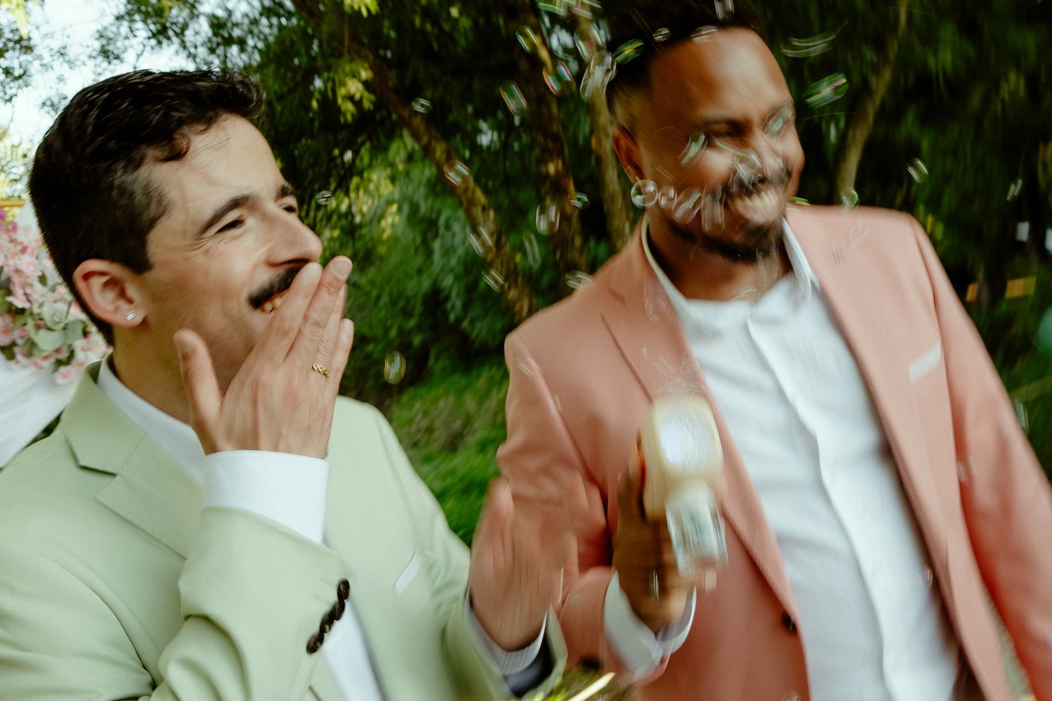 Two men in pastel suits laughing and celebrating outdoors at a festive event.