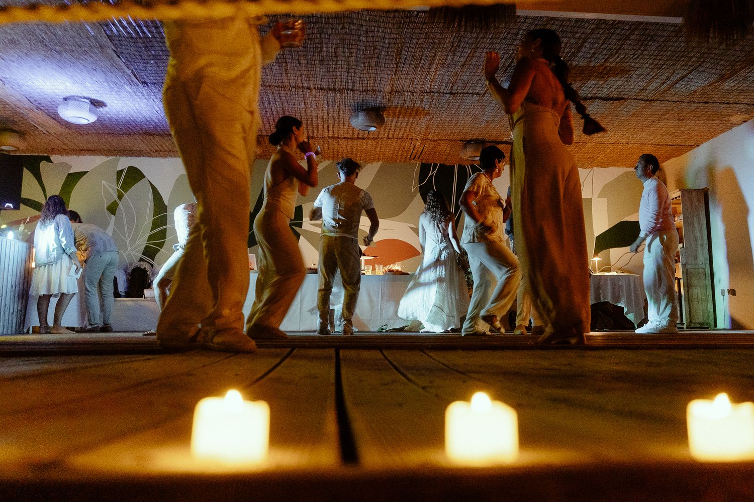 People dancing by candlelight in a warmly lit venue with candles glowing in the foreground.