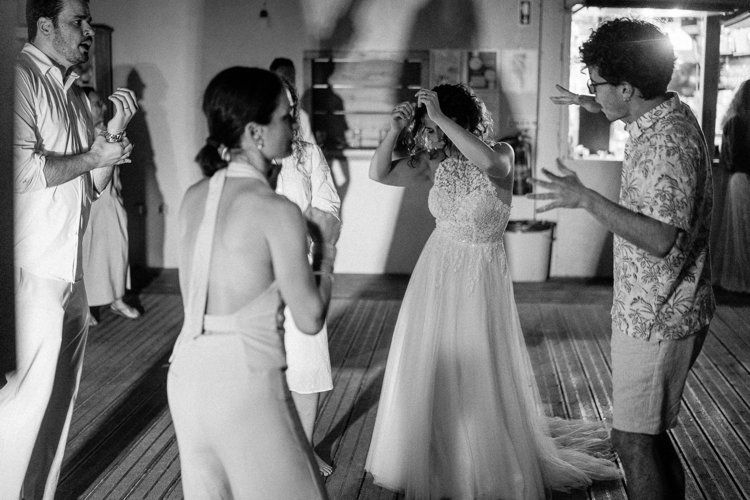 Black and white wedding photo of bride and guests dancing and celebrating at an indoor reception venue.