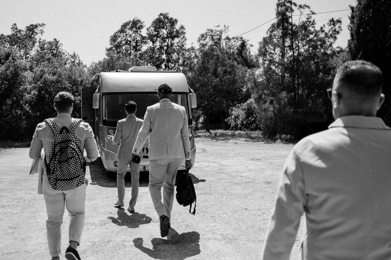Black and white photo of three people walking toward a vintage van on a sunny day outdoors.