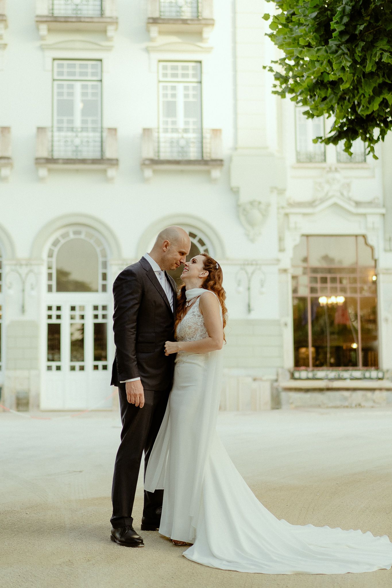 Bride and groom share a romantic kiss outside an elegant white European building on their wedding day.