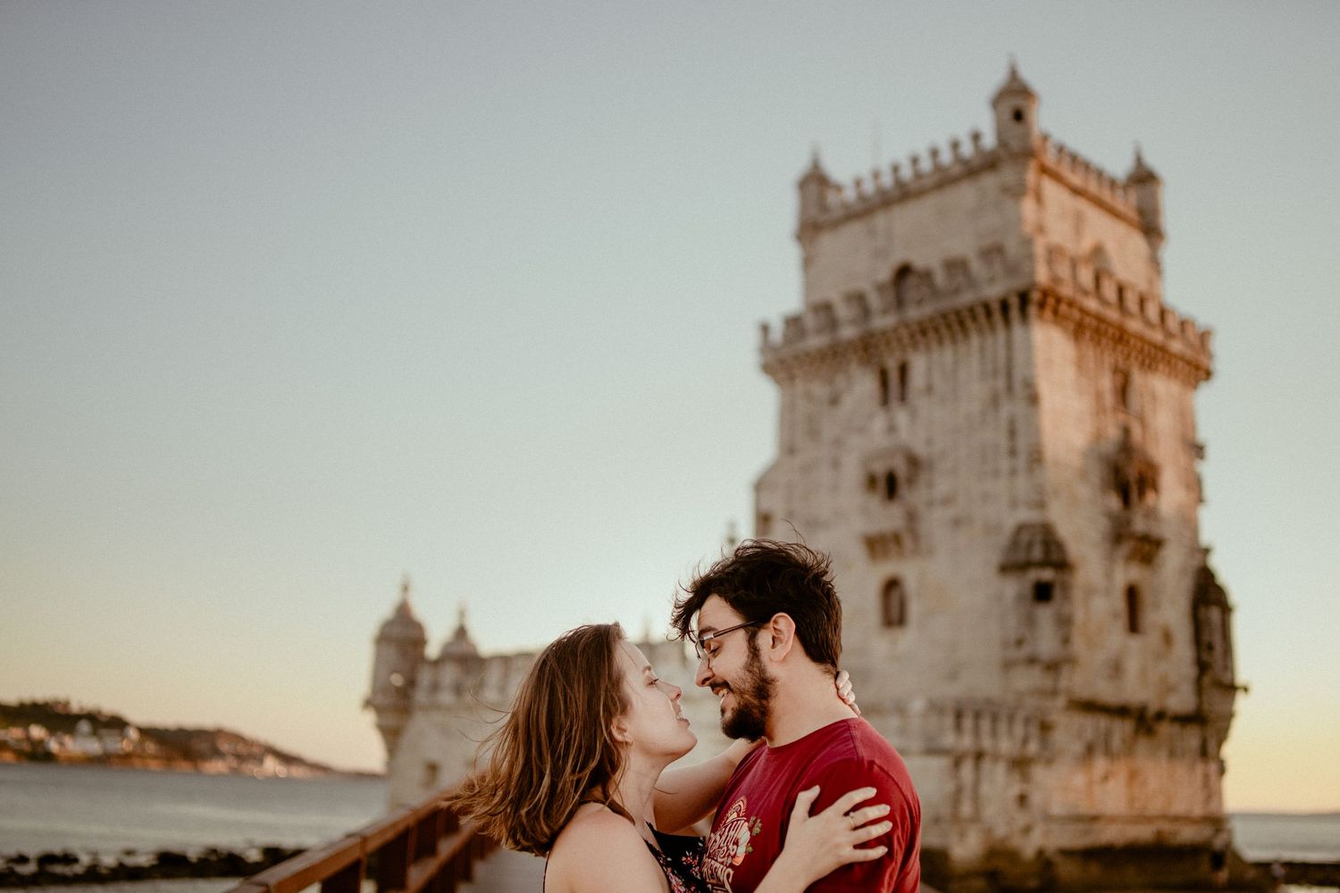 A couple embraces in front of historic Belem Tower in Lisbon during golden sunset light.