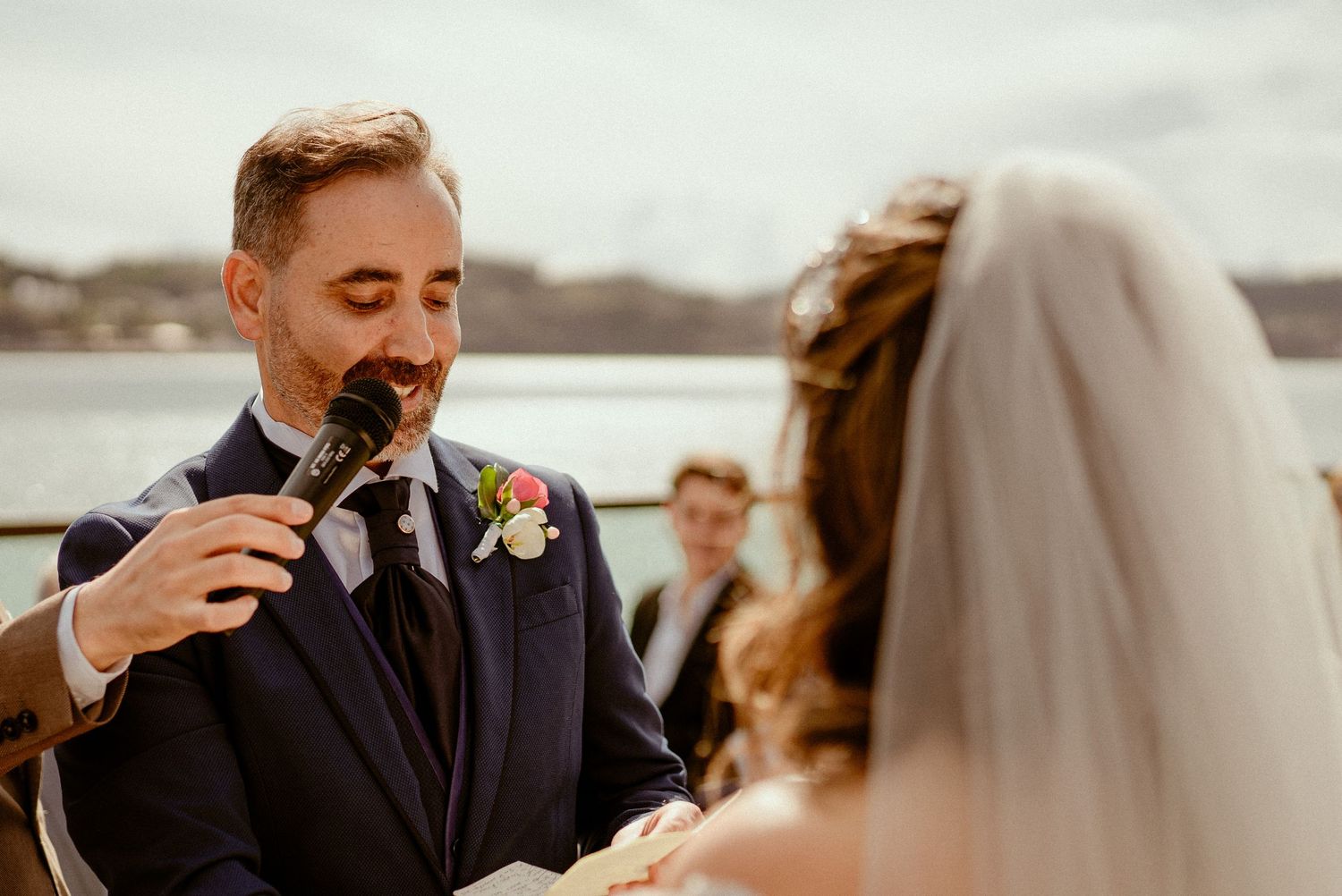 Two people embrace during an emotional wedding ceremony at an outdoor beachfront venue.