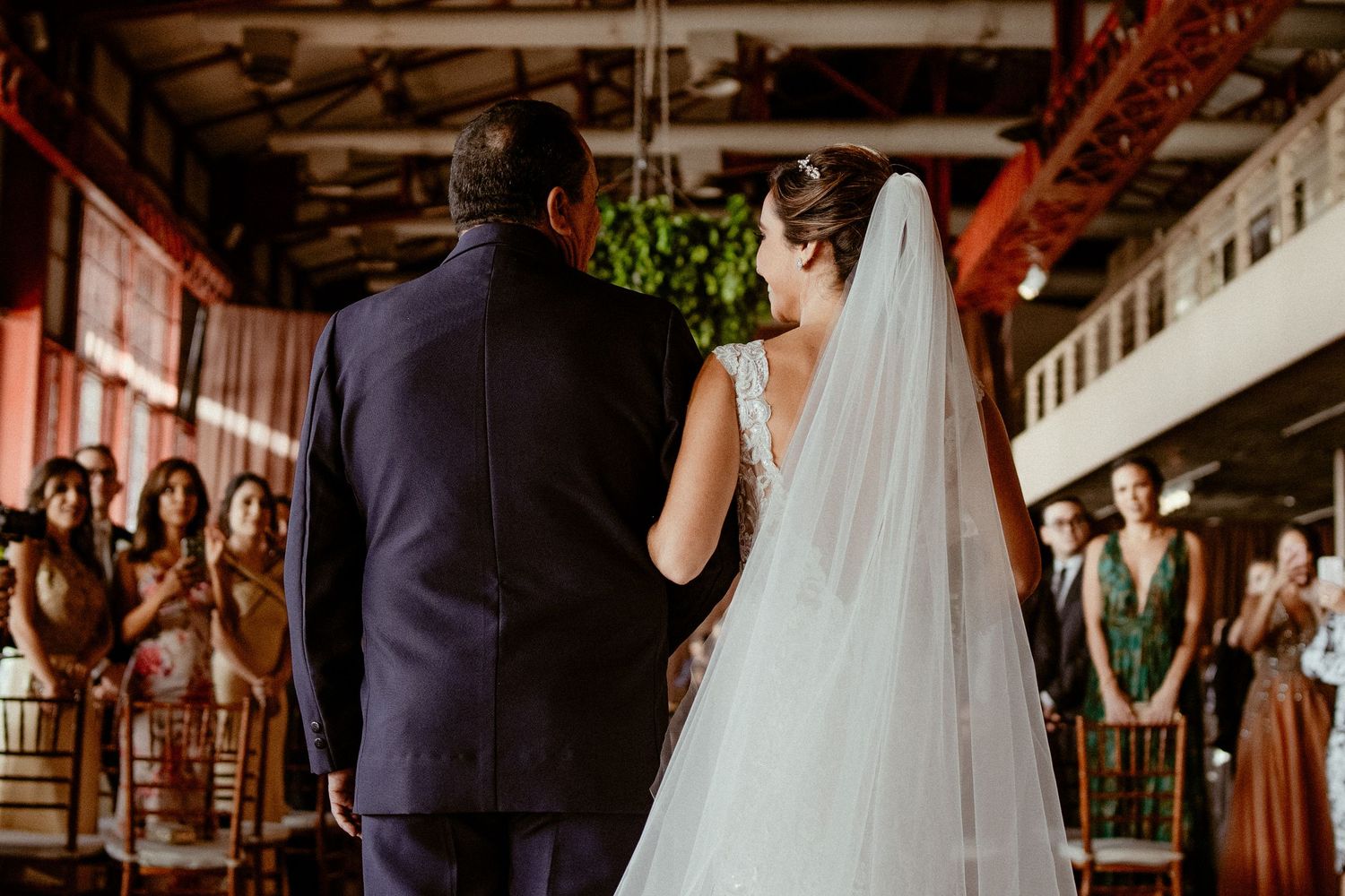 Wedding couple stands at altar during indoor ceremony while guests look on from rustic venue seating.