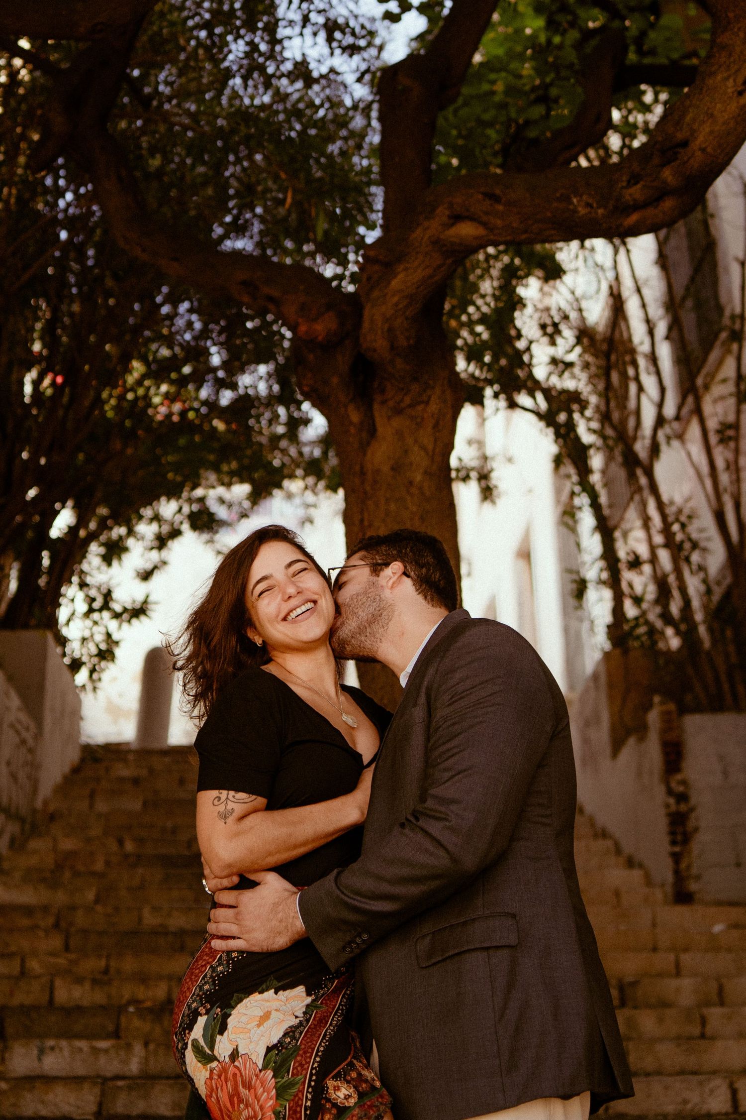 A couple shares intimate moments in a romantic outdoor photoshoot against a stone wall and trees.