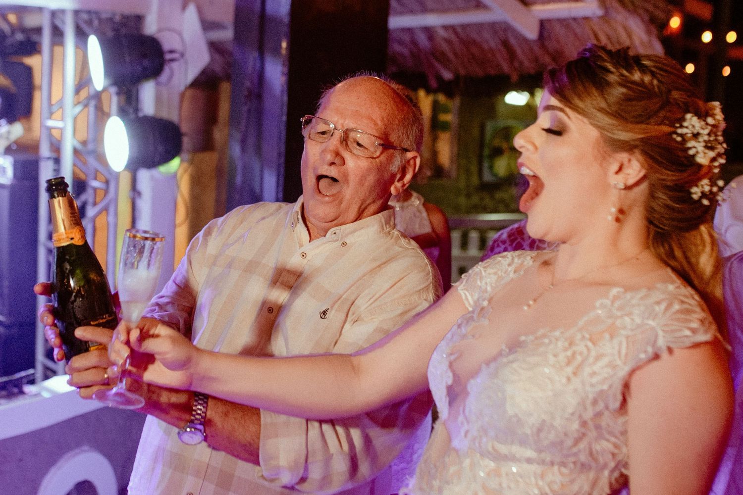 Wedding party celebrating with guests at reception, laughing and raising glasses during a toast.
