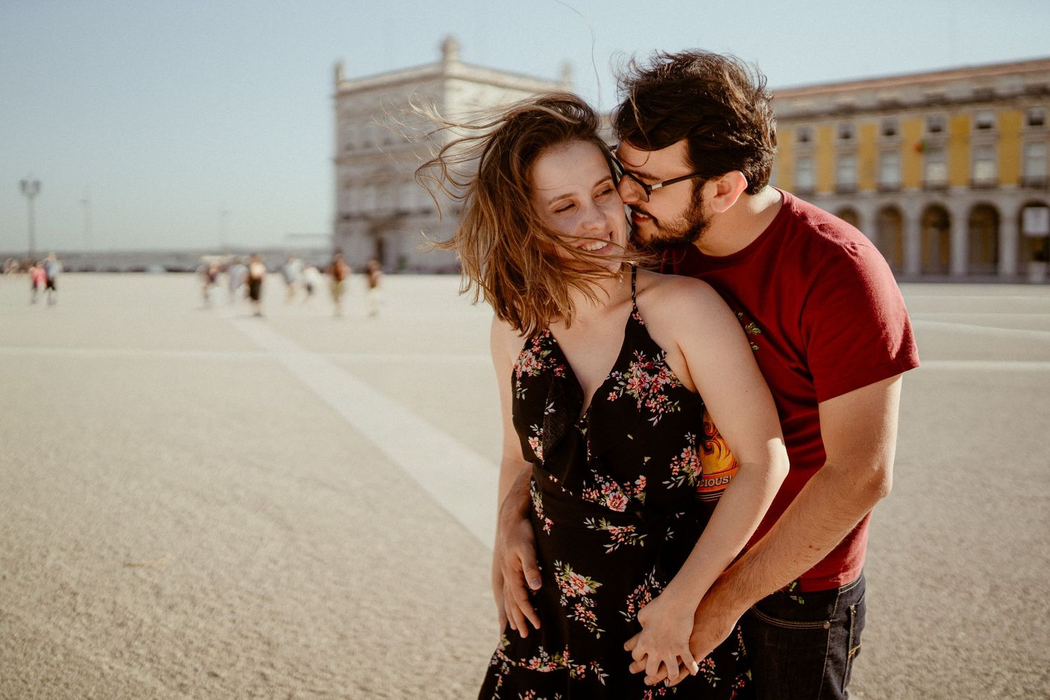A couple shares intimate moments while enjoying a sunny day in a historic town square.