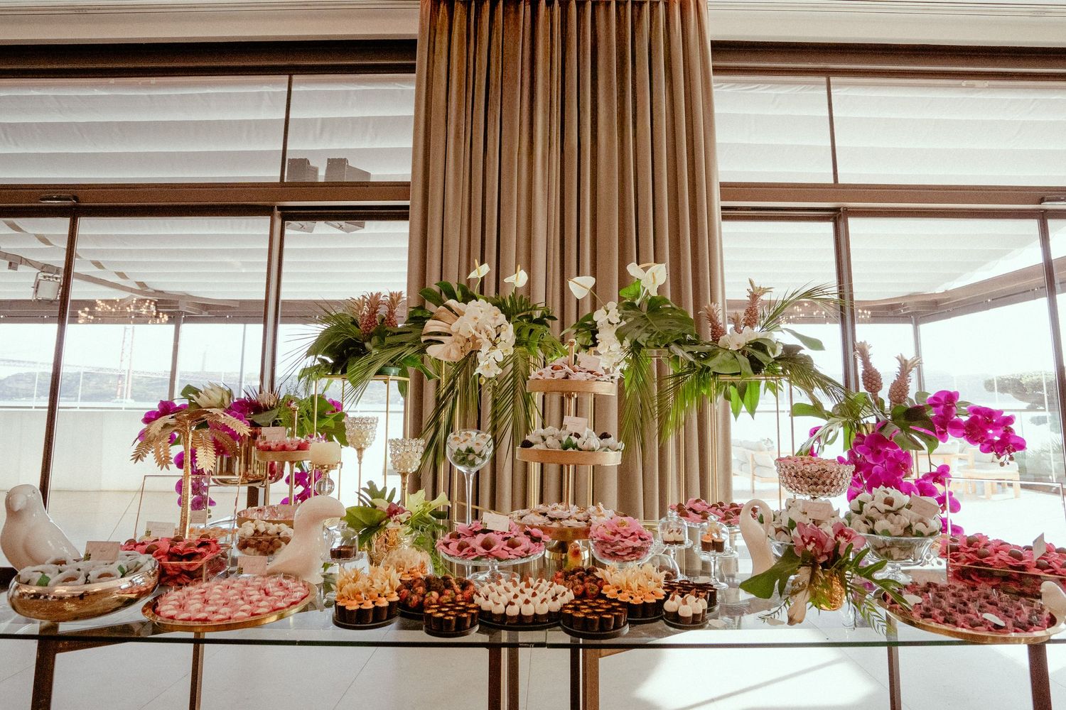 Elegant wedding reception venue decorated with crystal chandeliers and pink floral arrangements along the ceiling.