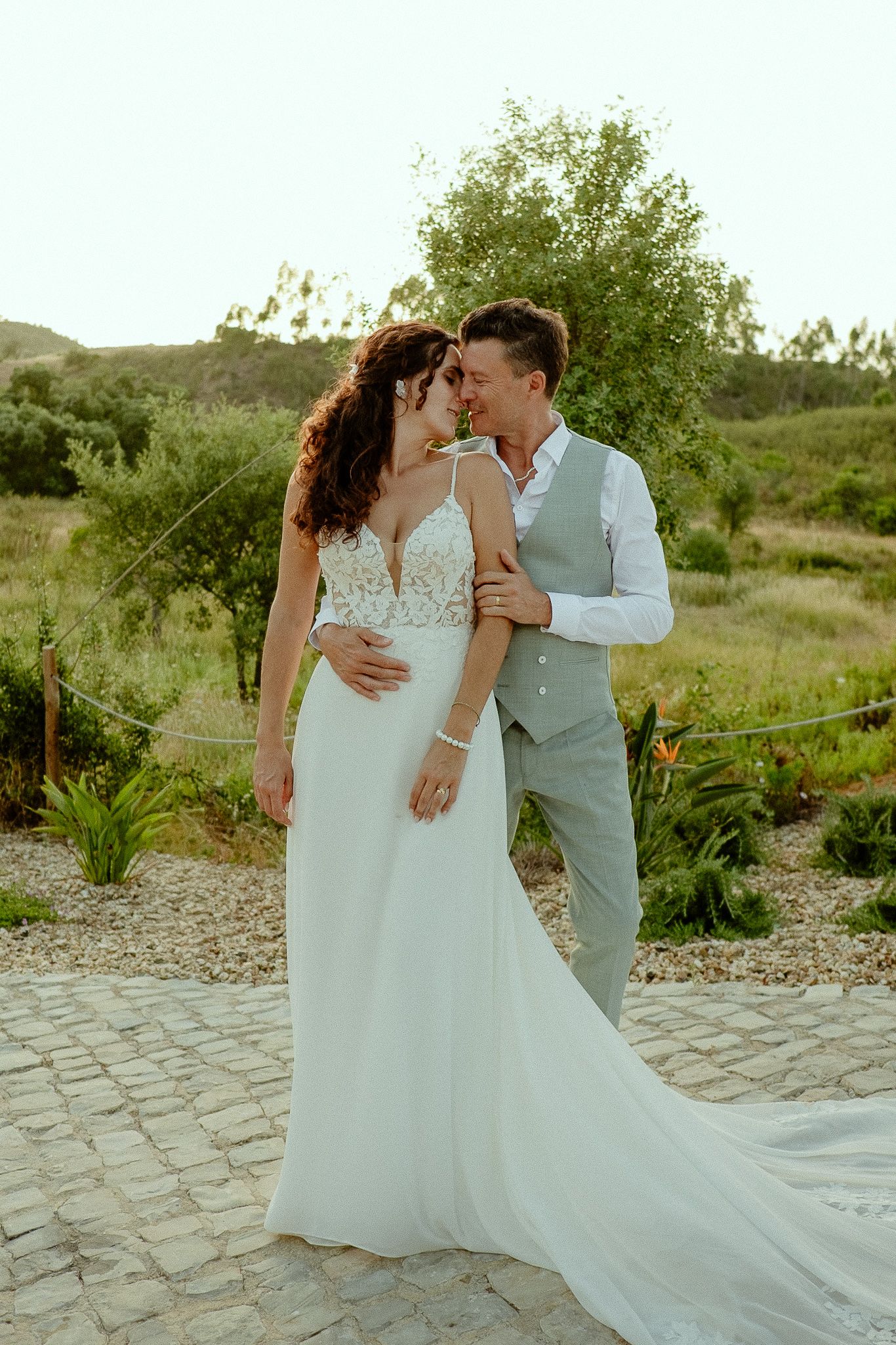A bride and groom share a romantic moment outdoors, with the bride in a white gown and groom in a gray suit.