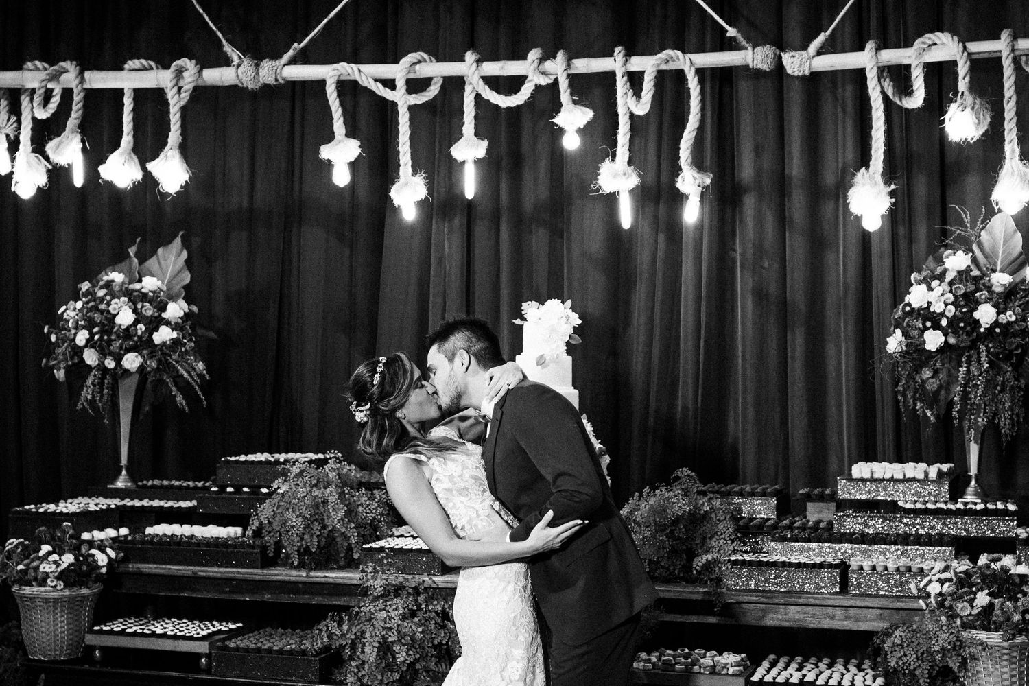 A black and white wedding photo with string lights and floral decorations creating an intimate dance atmosphere.