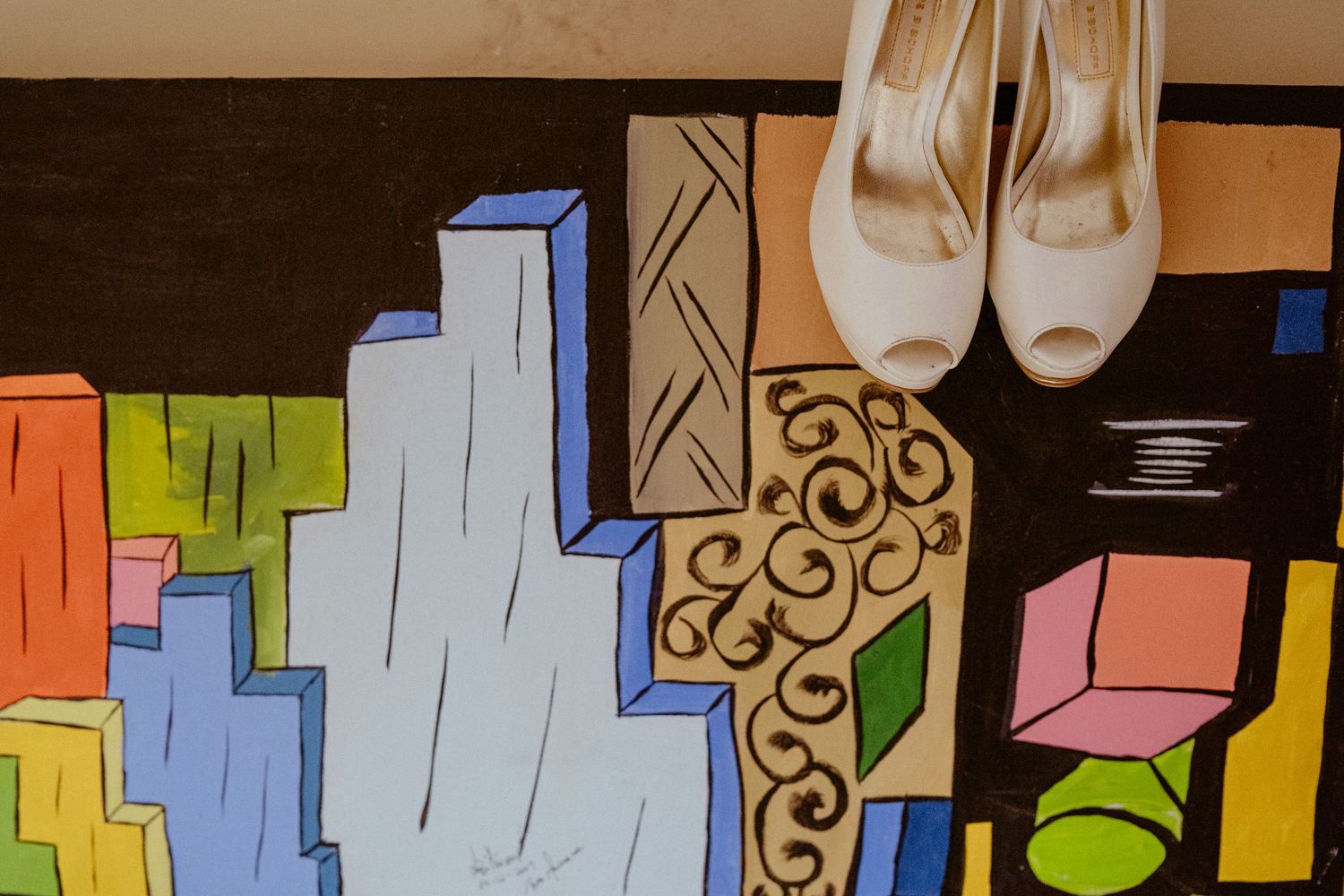 White bridal shoes displayed against a colorful geometric art background with blue and yellow shapes.