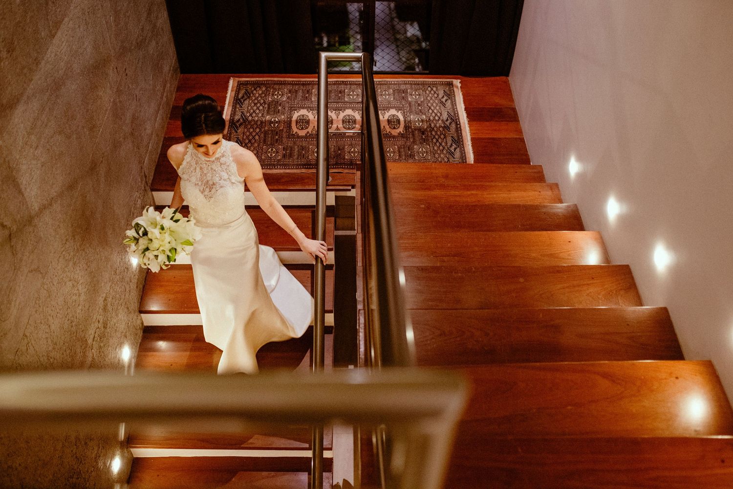 An elegant white wedding dress flows down illuminated wooden stairs in a romantic indoor setting.