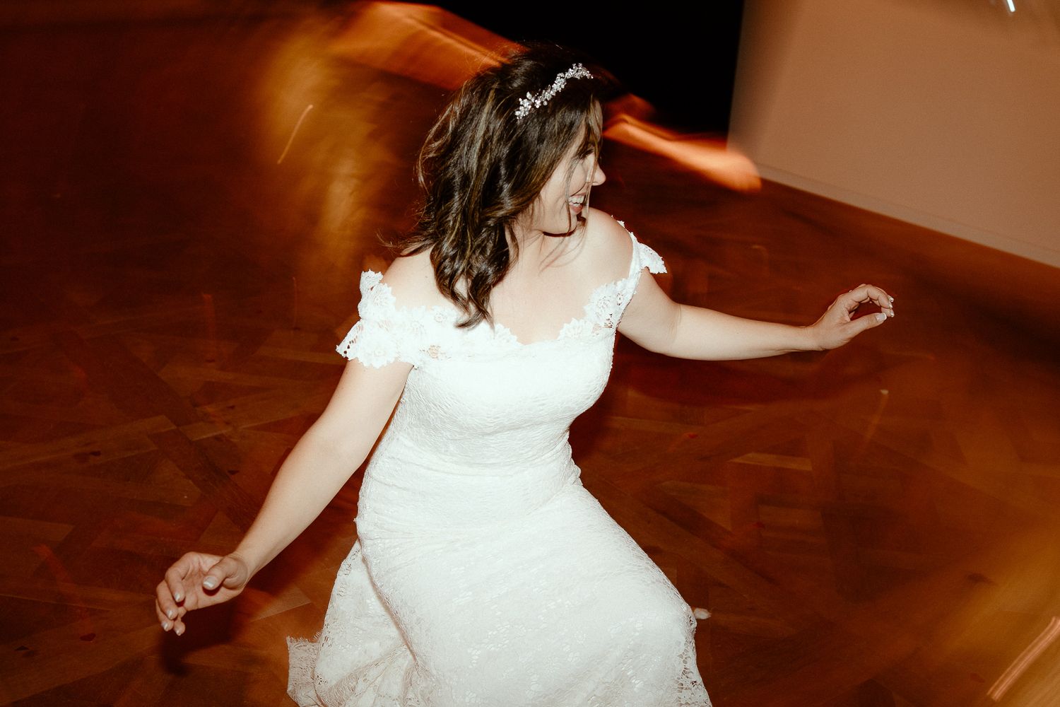 A person in a white wedding dress twirls on a wooden dance floor creating a motion blur effect.