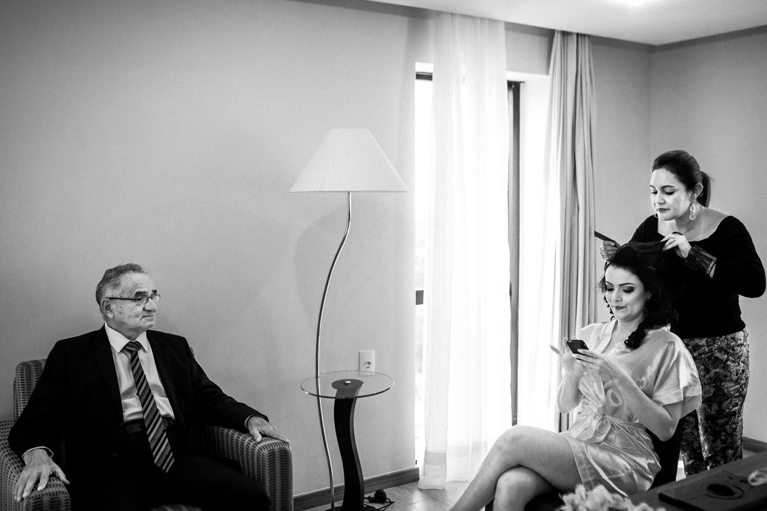 Black and white photograph capturing a quiet moment during wedding preparations in a hotel room.