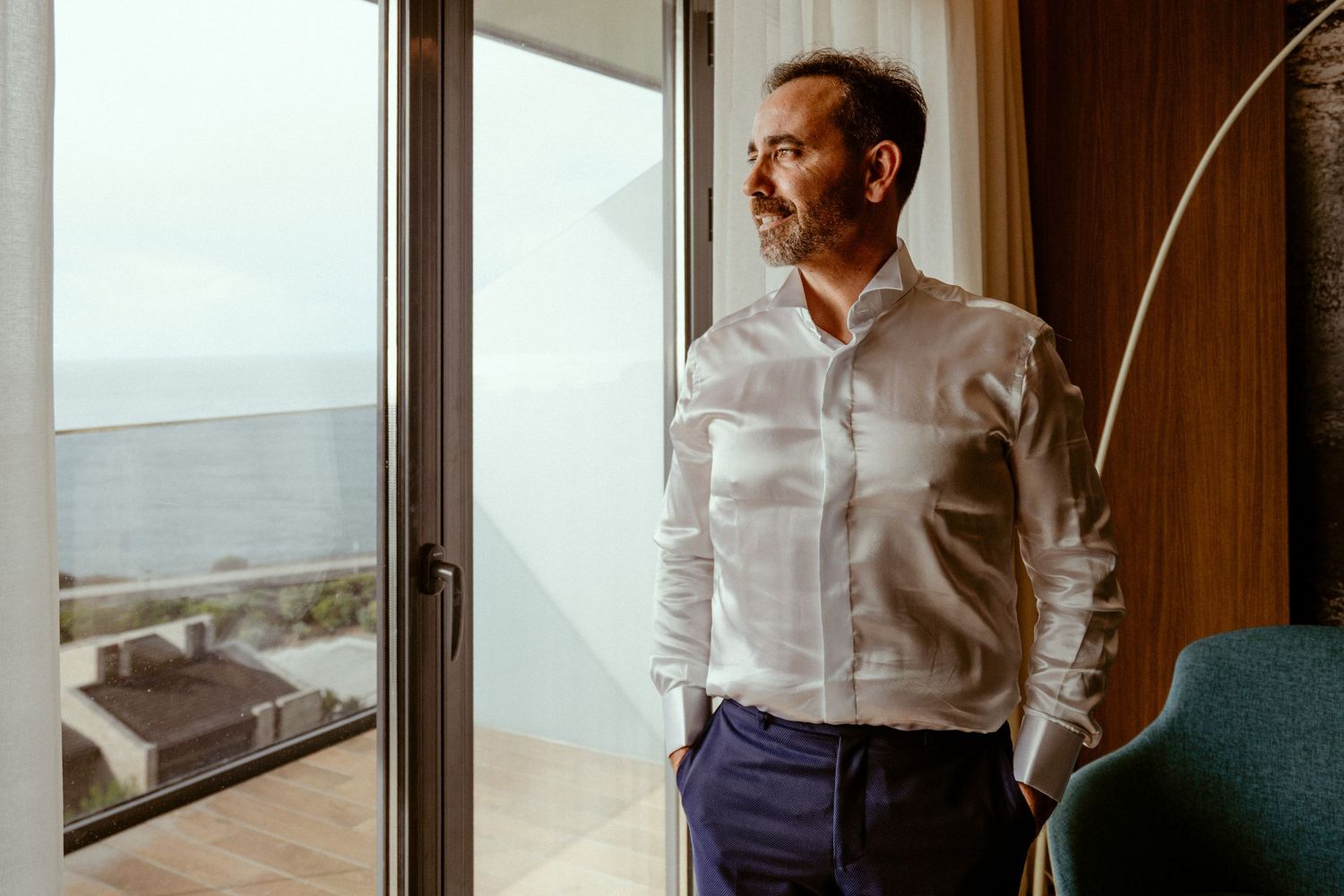 Professional in white shirt looking thoughtfully through window in modern apartment.