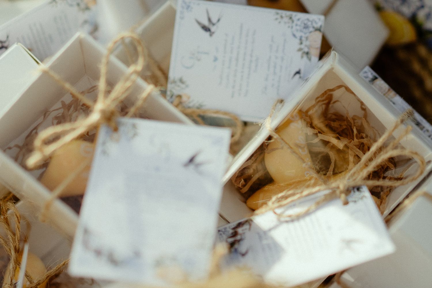 Elegant wedding favor boxes with twine bows, macarons, and decorative cards on rustic straw bedding.