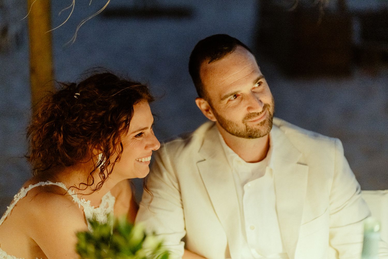 Bride and groom in white attire share a joyful moment at their outdoor evening wedding reception.