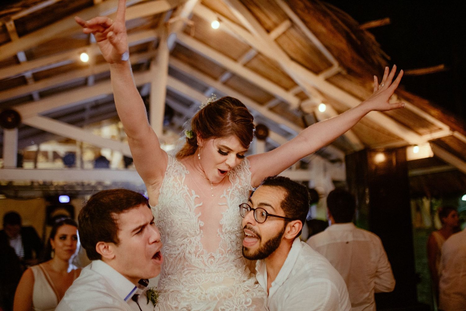 Wedding guests dancing joyfully and celebrating on a lively dance floor at an indoor reception.