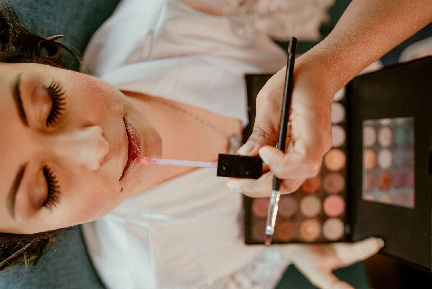Hands applying makeup using various cosmetic brushes and tools for beauty application.