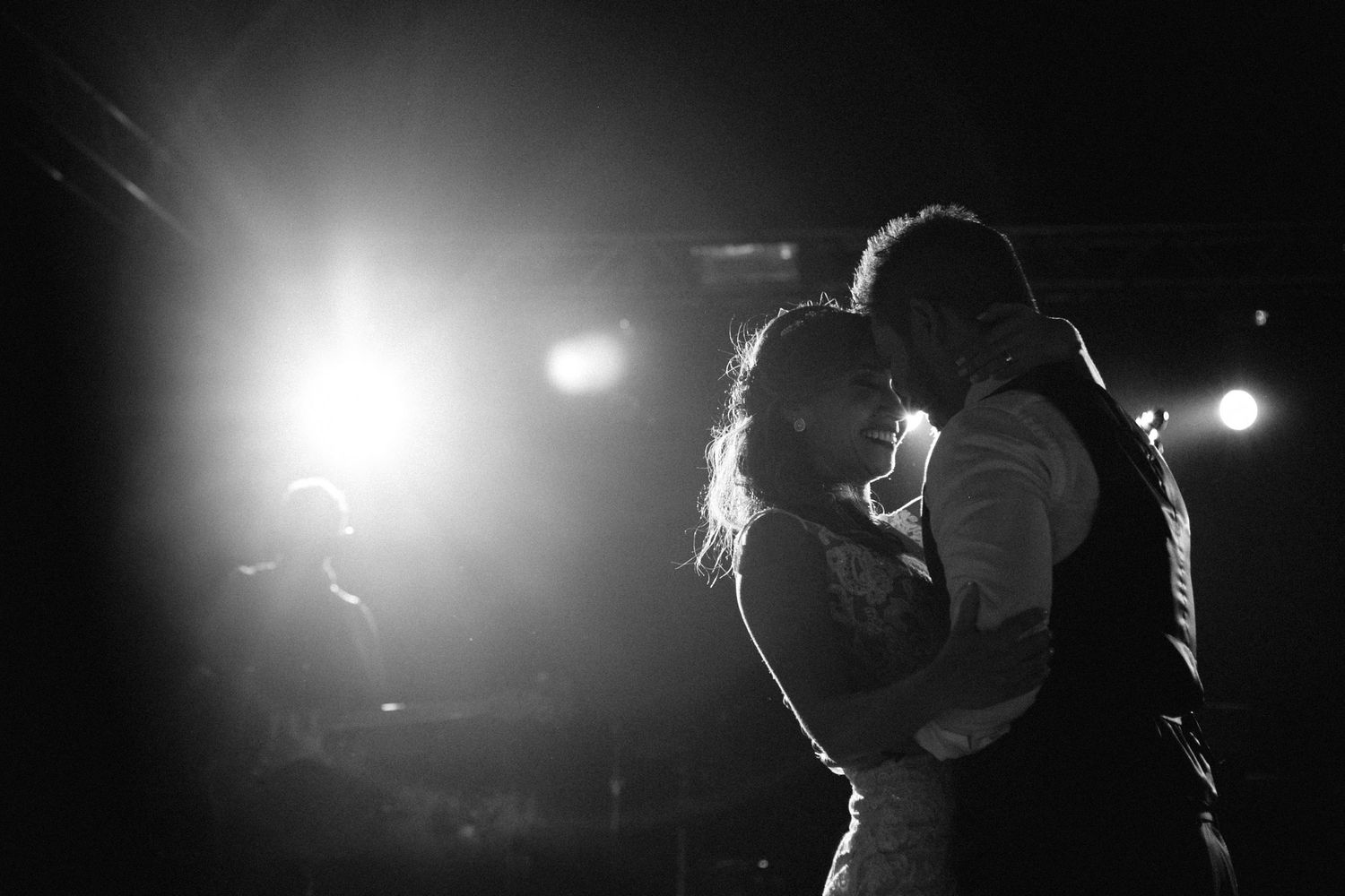 Dramatic silhouette of performers and bright spotlights on a dark stage during a live concert performance.
