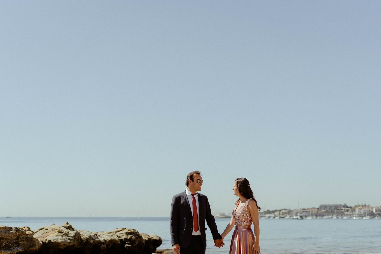 A couple stands together on a rocky beach overlooking the ocean during a sunset photo session.