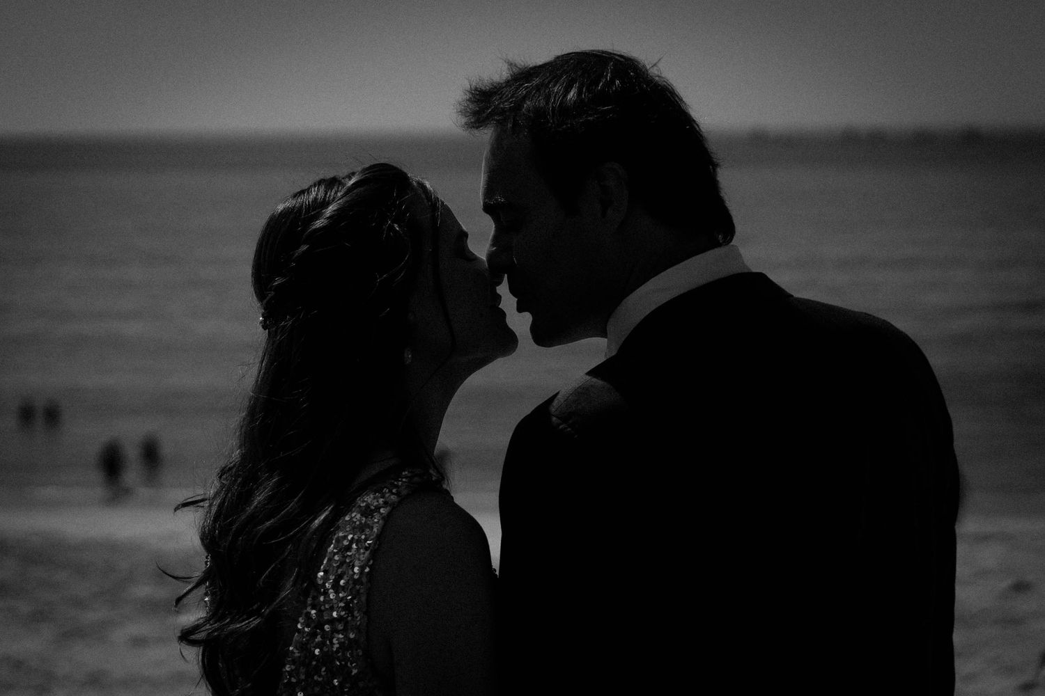 A romantic silhouette of a couple embracing on the beach at sunset in black and white.