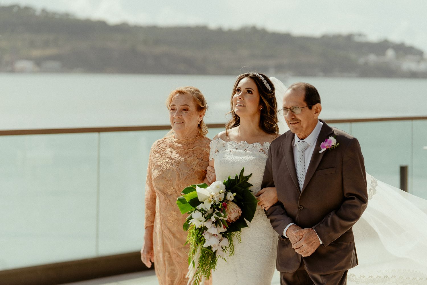 A wedding party stands together on a waterfront deck with scenic ocean views in the background.
