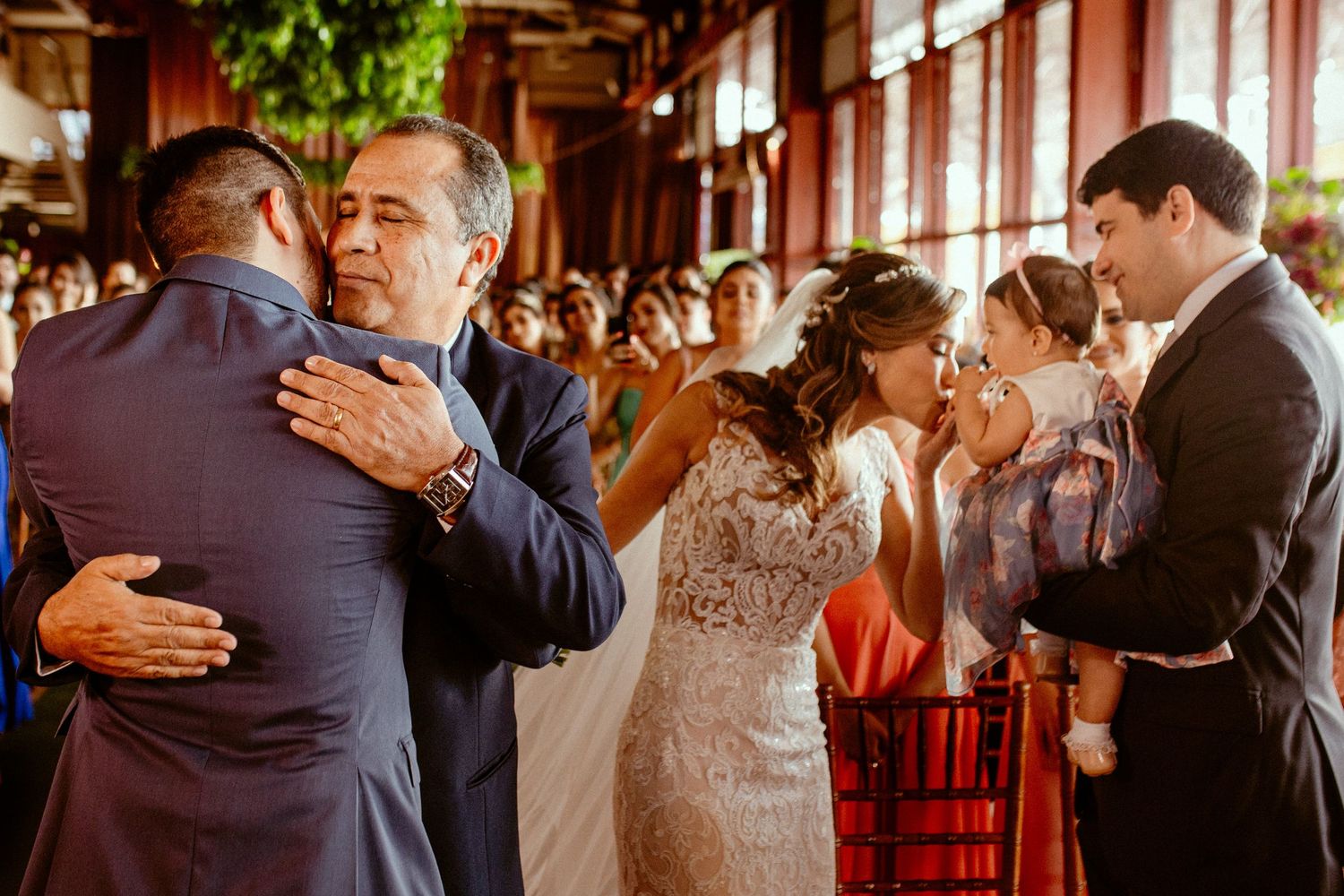 Wedding guests and family members embrace during an emotional reception celebration.