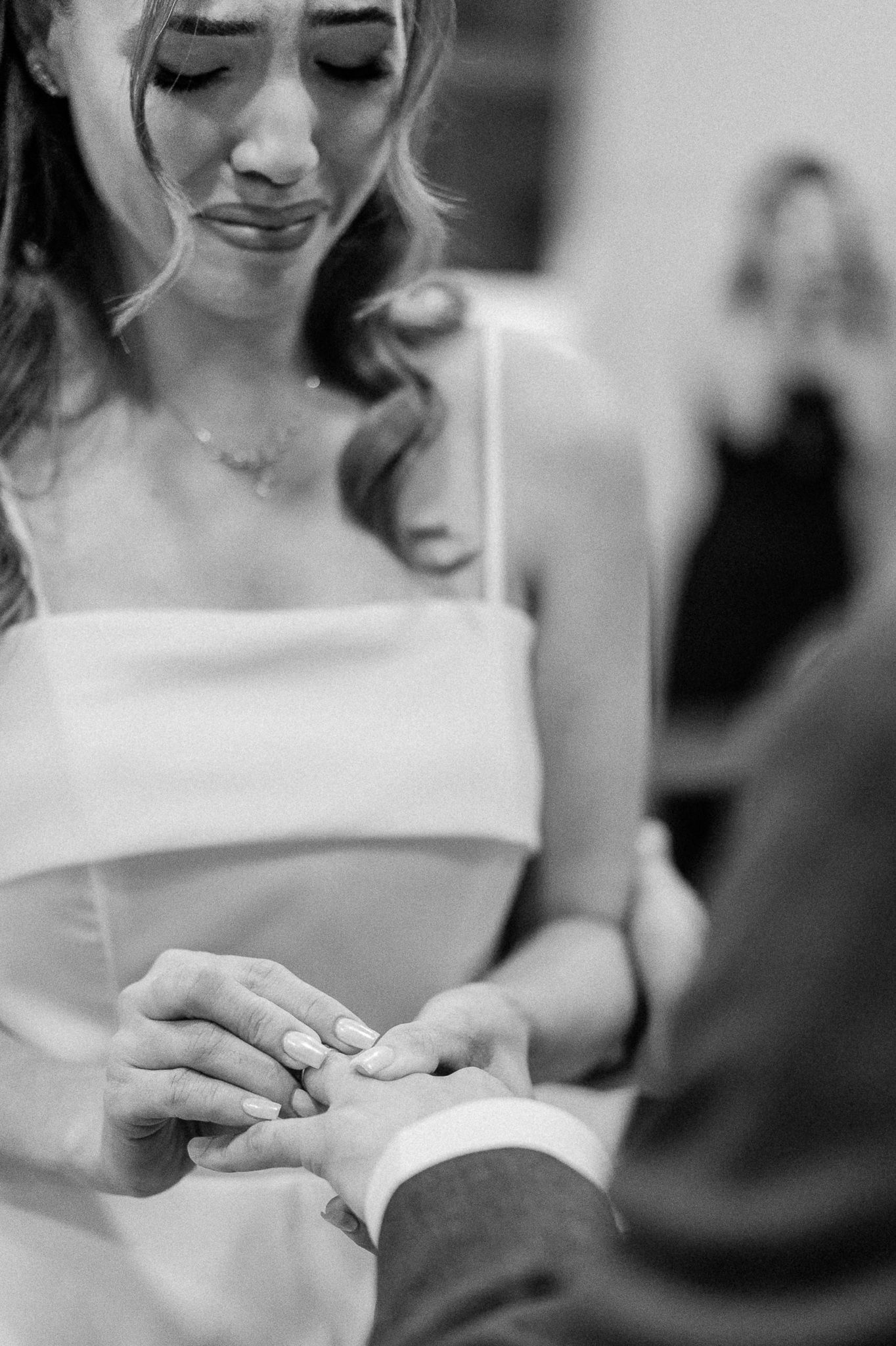 Black and white photo of emotional bride placing wedding ring on grooms hand during heartfelt ceremony exchange.
