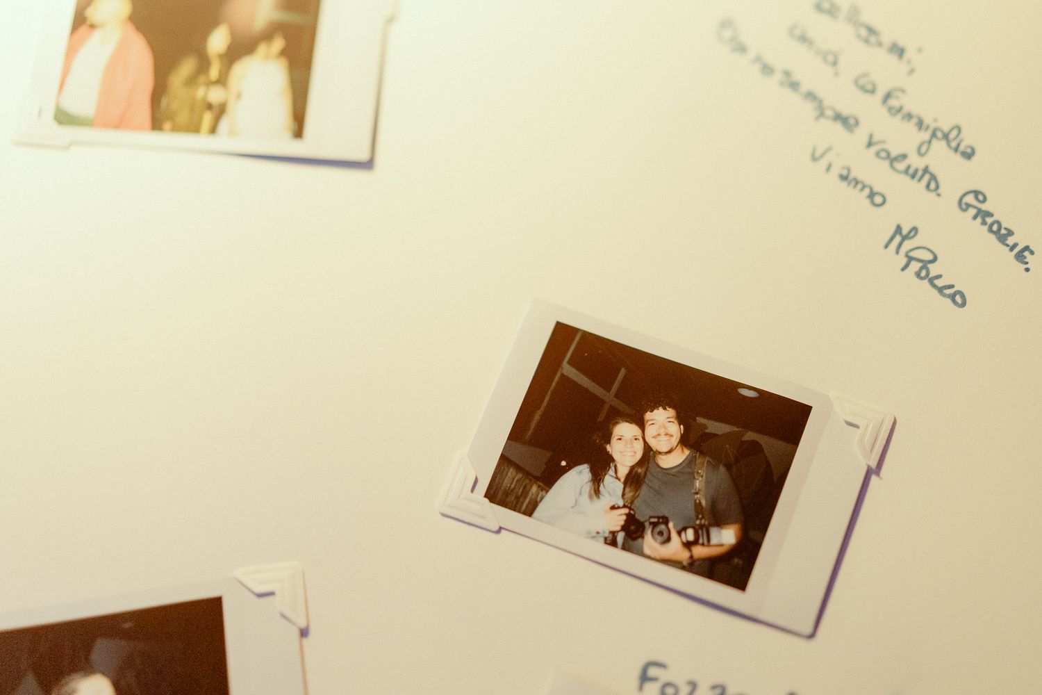 Polaroid photos of a smiling couple pinned on a white wall with handwritten notes in Italian.